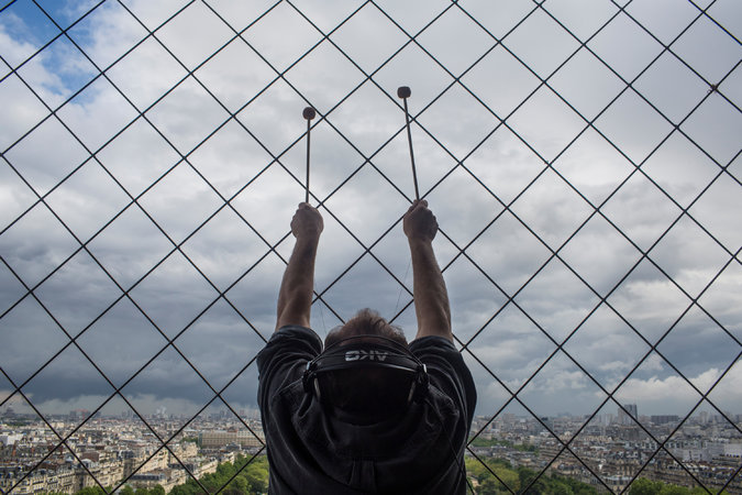 Still of a man hitting mallets against the Eiffel Tower in "Turning The Eiffel Tower Into A Musical Instrument"|Joseph Bertolozzi & Paul Kozel turning the Eiffel Tower into a musical instrument. Featured in our Weekly Flavor!