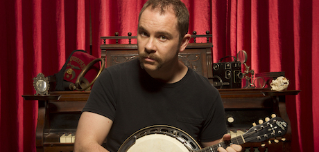 Picture of Producer's Toolbox composer Silas Hite sitting in front of a piano holding a banjo.|||Headshot of Producer's Toolbox composer Silas Hite holding a banjo in front of a piano.||||||