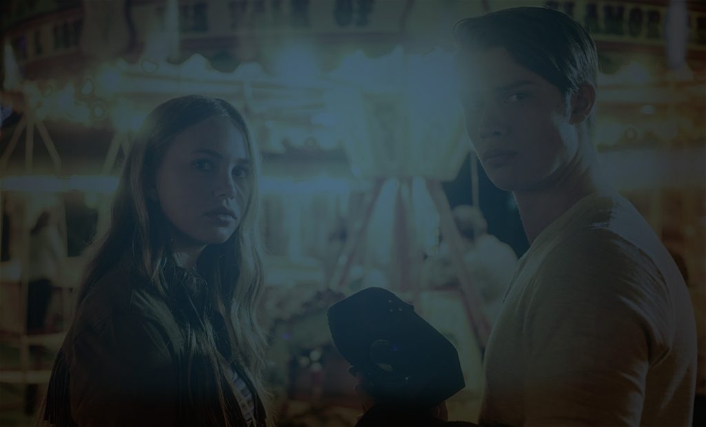 Still of two people in front of a carousel from Lifetime TV remake of The Watcher In The Woods starring Anjelica Houston. Flavorlab Sound provided full service audio post for the film: sound design and mix.|